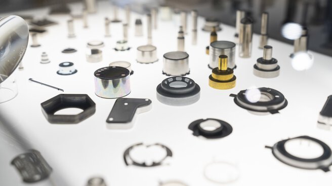 Auf einem weißen Leuchttisch sind verschiedene präzise gefertigte Bauteile ausgestellt.