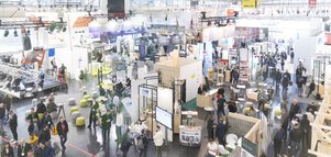Weitwinkelansicht einer gut besuchten Messehalle mit zahlreichen Ausstellungsständen, Infotafeln und Besuchergruppen in Gesprächen.