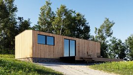 Moderne Holzhütte mit großen Fenstern, inmitten einer Grasfläche mit umgebenden Bäumen unter einem klaren blauen Himmel.