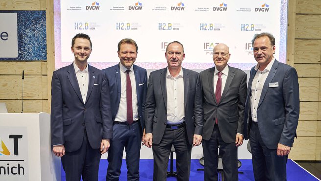 Five men in suits pose shoulder to shoulder in front of a logo wall on an IFAT Munich stage.