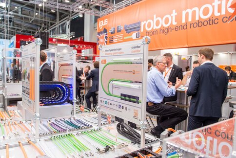 People are talking at a booth at a tech fair where robot cables and cable management systems are on display.