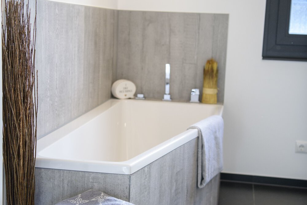 Modernes Badezimmer mit Eckbadewanne, hellgrauen Fliesen und einem über dem Rand hängenden weißen Handtuch.