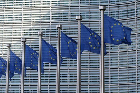 Several EU flags fly in front of a modern building with a lattice-like façade.