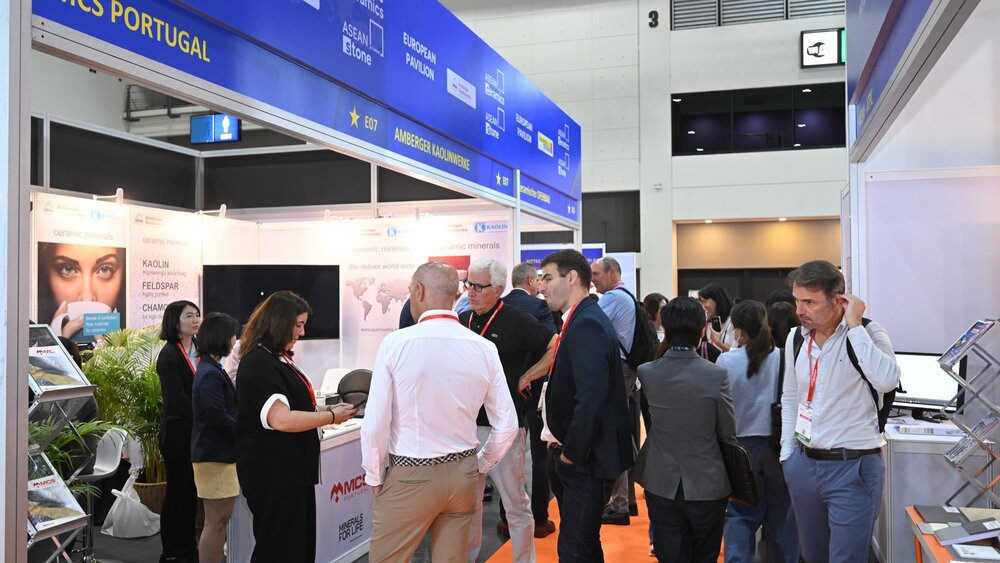 A few exhibition stands at a ceramitec event, with several visitors and exhibitors standing in groups between them.