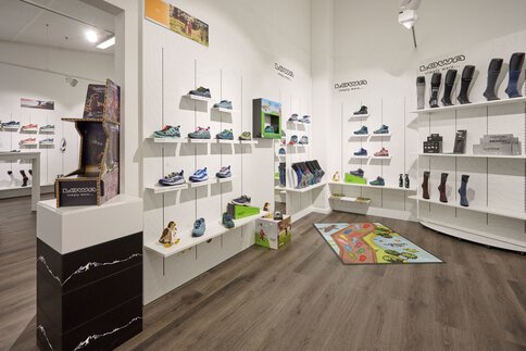 Schuhladen mit Regalen mit bunten Sportschuhen, Stiefeln und Socken auf einem Holzboden.