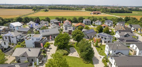 Luftaufnahme des Bauzentrum Poing mit Häusern, grünen Rasenflächen und umliegenden Feldern unter klarem Himmel.