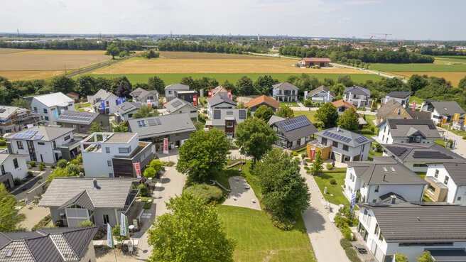 Luftaufnahme des Bauzentrum Poing mit Häusern, grünen Rasenflächen und umliegenden Feldern unter klarem Himmel.