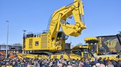 Large yellow mining excavator from Komatsu in front of a crowd.