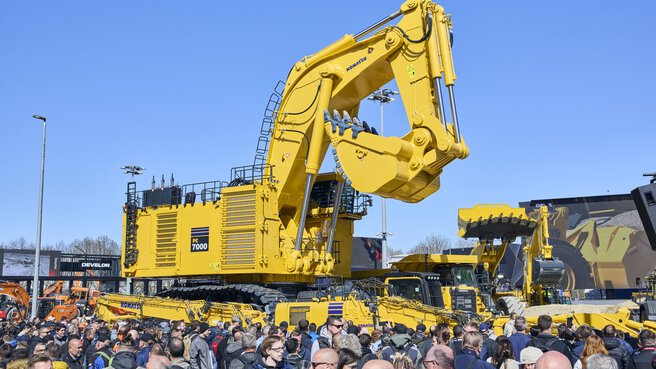 Large yellow mining excavator from Komatsu in front of a crowd.