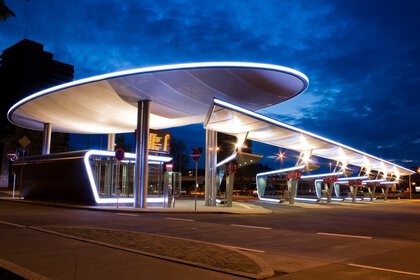 Futuristischer, beleuchteter Busbahnhof mit ovalen Dächern vor einem tiefblauen Abendhimmel.