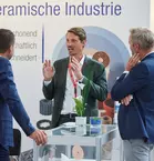 Three men in suits discussing at a glass table at bauma.