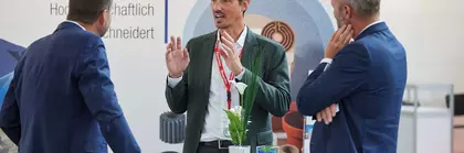 Drei Männer im Anzug diskutieren an einem Glastisch auf der bauma.