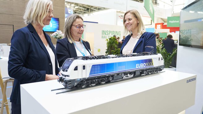 Three ladies marvel at Stadler's EURO9000 train model at transport logistic 2025.