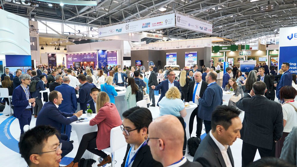 Numerous visitors to transport logistic Americas sit and stand at tables in the networking area and chat.
