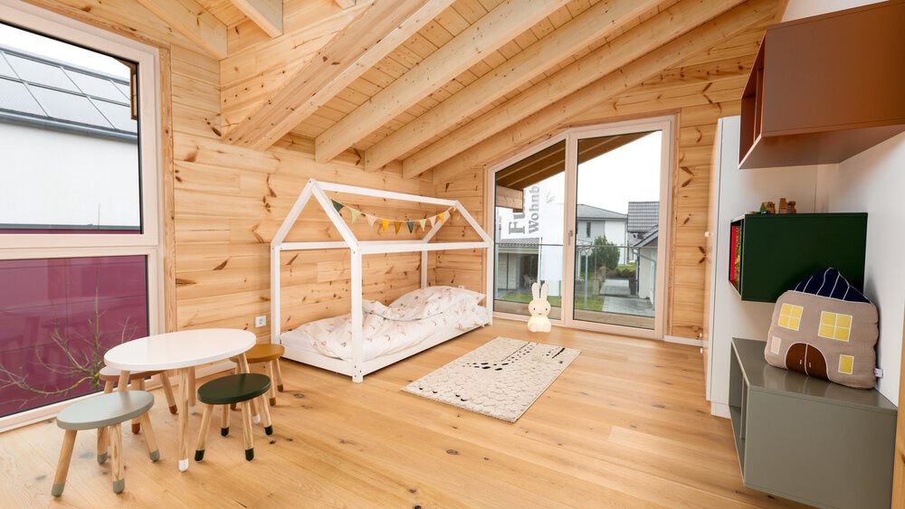 Kinderzimmer mit großem Fenster, weißem Bettgestell in Spielhausform, kleinem runden Tisch mit passenden Stühlen, Hängeregalen in gedeckten Erdtönen und großer Balkontür.