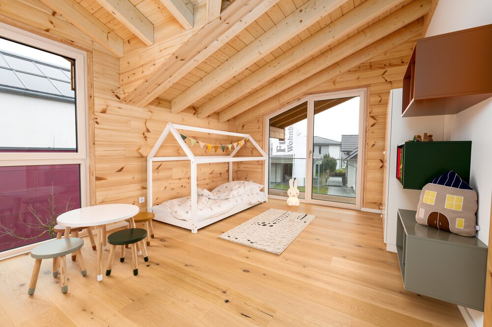 Kinderzimmer mit großem Fenster, weißem Bettgestell in Spielhausform, kleinem runden Tisch mit passenden Stühlen, Hängeregalen in gedeckten Erdtönen und großer Balkontür.