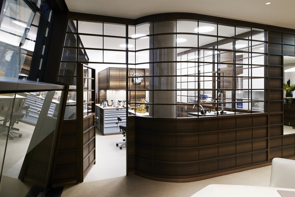 Modernes Büro mit glas- und holzvertäfelten Wänden, Schreibtischen, Stühlen und einem gut beleuchteten, organisierten Arbeitsbereich im Inneren.