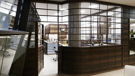 Modernes Büro mit glas- und holzvertäfelten Wänden, Schreibtischen, Stühlen und einem gut beleuchteten, organisierten Arbeitsbereich im Inneren.