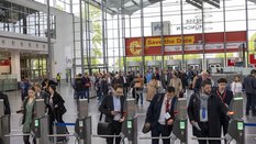 Eine gut besuchte Messe mit Warteschlangen am Eingang und einem großen bunten Schild am Eingang.