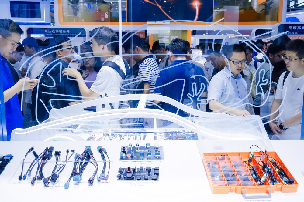 Auf einer Ausstellung werden elektronische Autokomponenten hinter einer Glasscheibe mit dem Umriss eines Autos gezeigt.