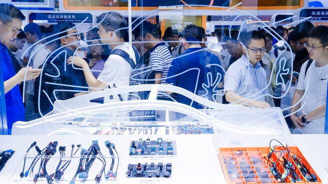 Auf einer Ausstellung werden elektronische Autokomponenten hinter einer Glasscheibe mit dem Umriss eines Autos gezeigt.