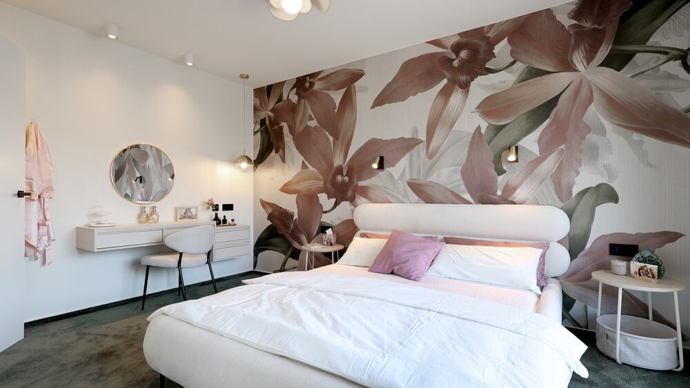 Modernes Schlafzimmer mit rosa Blumentapete, weißem Bett, runden Beistelltischchen und einem Frisiertisch mit rundem Spiegel.