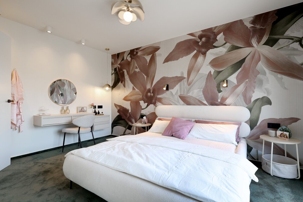Modernes Schlafzimmer mit rosa Blumentapete, weißem Bett, runden Beistelltischchen und einem Frisiertisch mit rundem Spiegel.