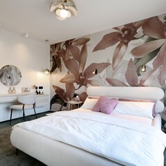 Modernes Schlafzimmer mit rosa Blumentapete, weißem Bett, runden Beistelltischchen und einem Frisiertisch mit rundem Spiegel.