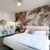 Modernes Schlafzimmer mit rosa Blumentapete, weißem Bett, runden Beistelltischchen und einem Frisiertisch mit rundem Spiegel.