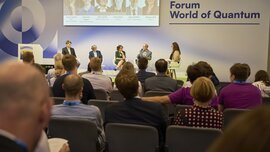 Podiumsdiskussion auf der Veranstaltung Forum World of Quantum, mit dem Publikum auf den Sitzen und den Rednern auf der Bühne.