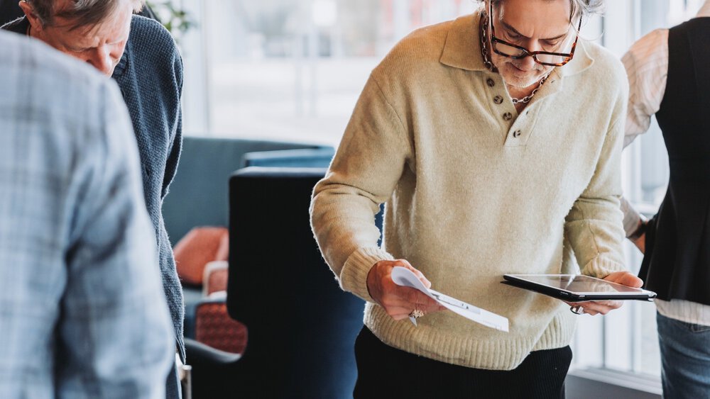 Several people are standing at a table looking at the wristwatches displayed there in black wooden boxes.