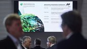 Blurred group of people in the foreground, behind them a display hangs on the wall showing the schedule of the electronica Automotive Conference.