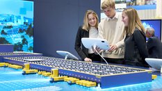 Zwei Frauen und ein Mann betrachten ein Logistikmodell zur emissionsfreien Zustellung am Tablet.
