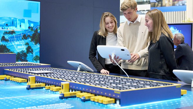 Two women and a man look at a logistics model for emission-free delivery on a tablet.