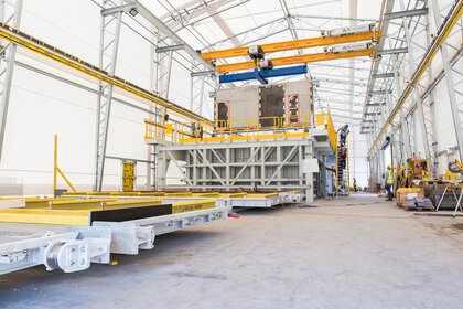 Große Industrieanlage im Innenbereich mit Kränen, Baumaschinen und Arbeitern im Hintergrund.