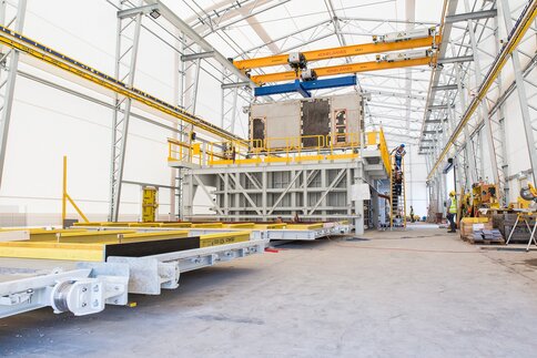 Große Industrieanlage im Innenbereich mit Kränen, Baumaschinen und Arbeitern im Hintergrund.