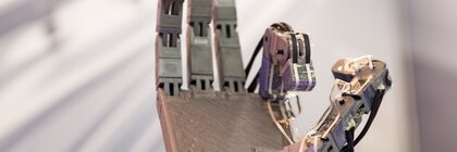 Close-up of a metallic robotic hand with bent thumb and index finger, against a blurred background.