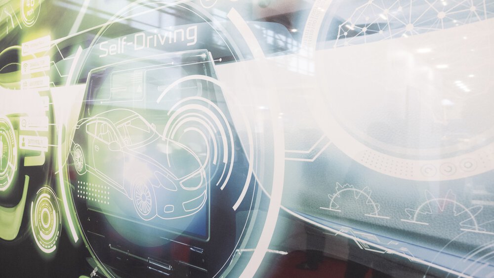 Glowing graphic on autonomous driving shows a stylized car and digital interface elements with the text Self Driving