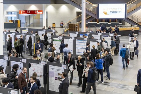 Zahlreiche Besucher stehen zwischen mehreren Reihen von Informationstafeln auf der LOPEC Messe und betrachten die angepinnten Poster.