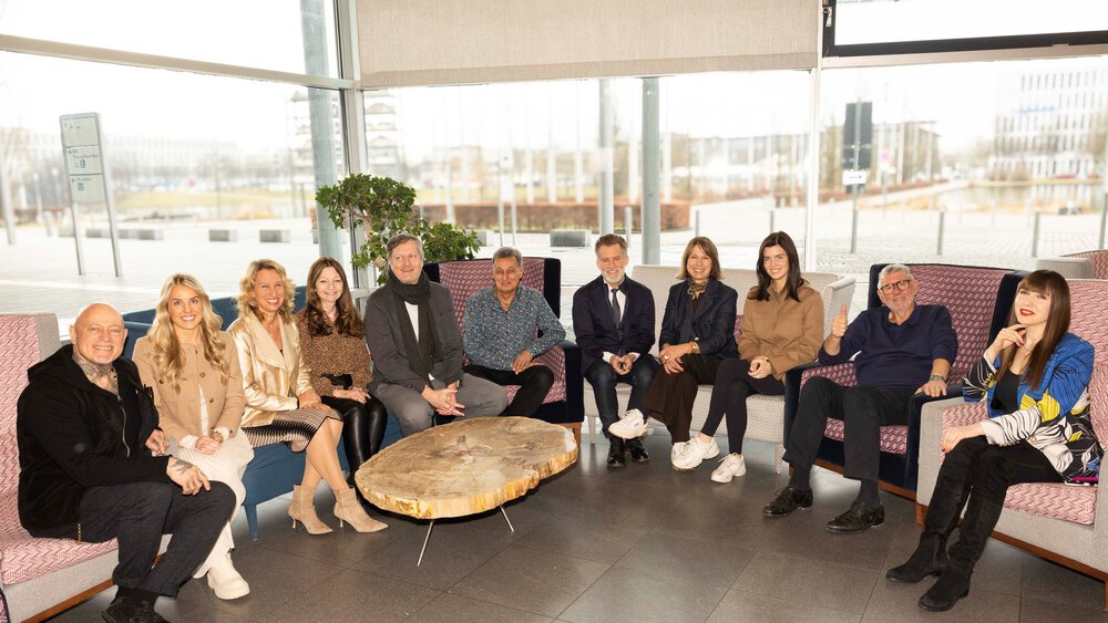 A group photo of people sitting together in a brightly lit room with a round wooden table in front of them.