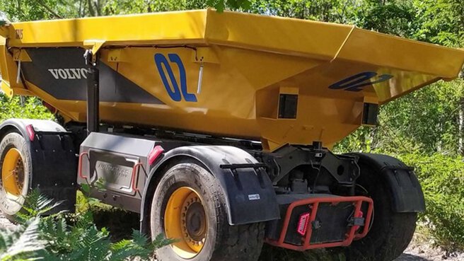 Gelber Volvo-Dumper mit großen Reifen und der Nummer 02, geparkt im Grünen.
