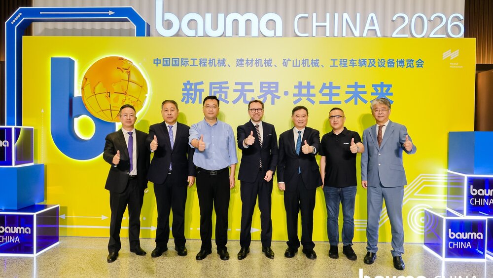Seven people in business attire are standing in front of a colourful backdrop at an event at bauma CHINA 2026, smiling and giving a thumbs-up.