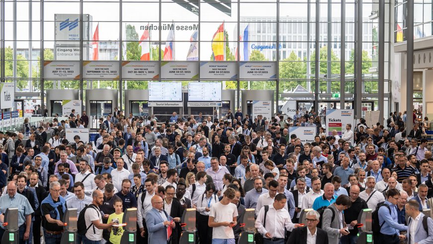 A large crowd gathers in front of the ticket barriers in the West Entrance Hall.