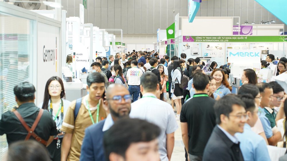 A large crowd walking through a busy exhibition hall with various stands and displays.