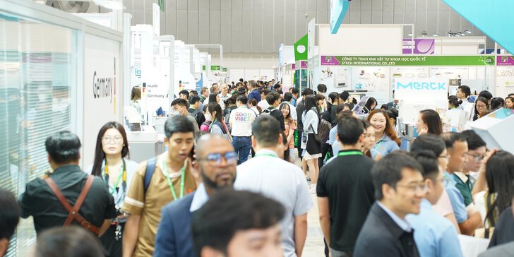 A large crowd walking through a busy exhibition hall with various stands and displays.