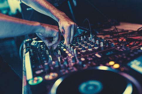 Nahaufnahme der Hände eines DJs, der bei einer Musikveranstaltung die Knöpfe eines Mischpults bedient.