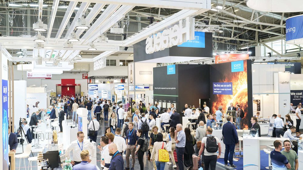 A busy trade fair with people walking along the various stands and exhibitions in a large exhibition hall.