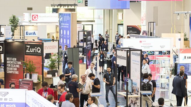 Blick auf die belebte Messehalle der World of Quantum in München mit zahlreichen Ausstellern und Besuchergruppen an den Ständen.