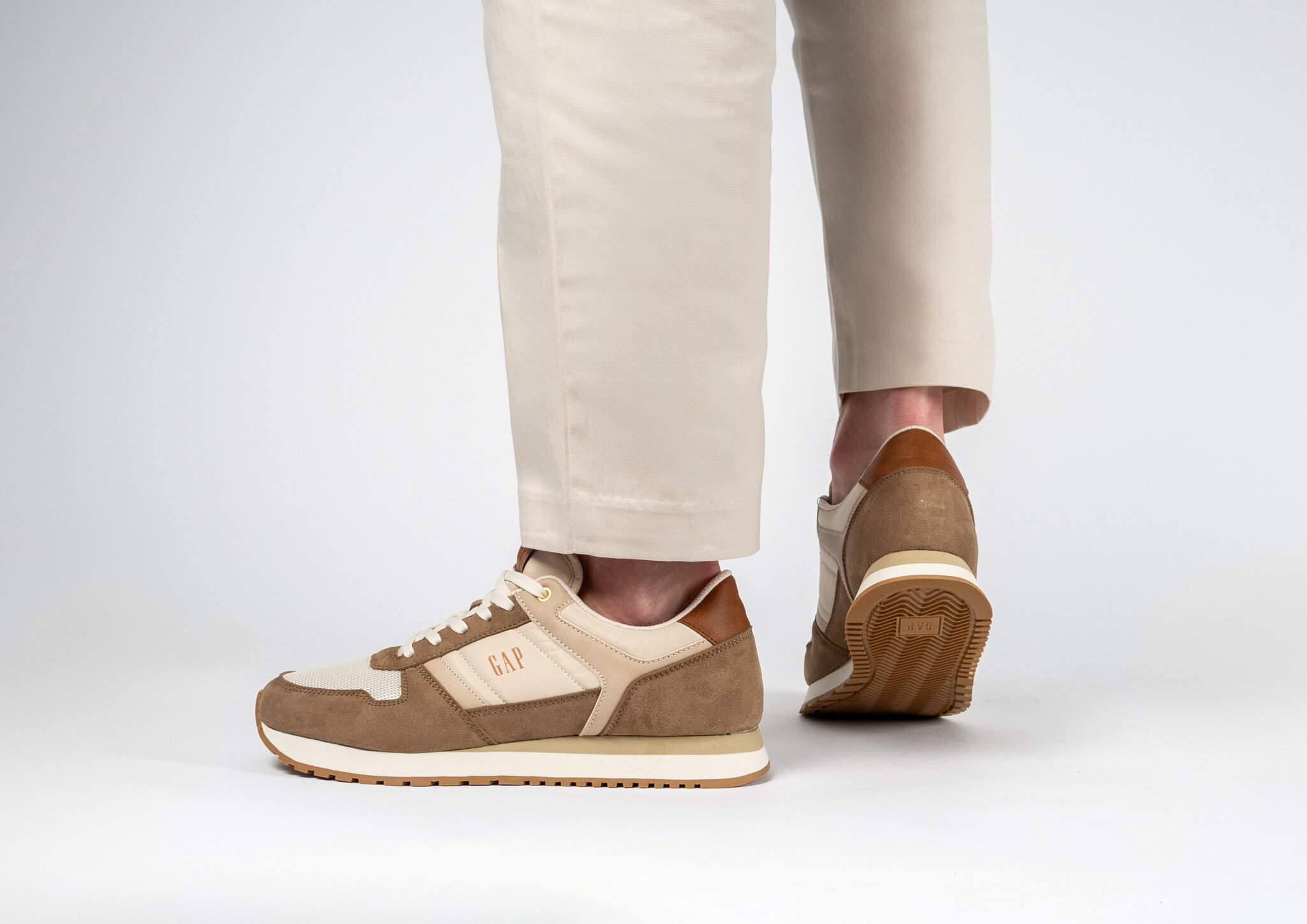 Ein Paar Beine in weißer Hose stecken in braun-beigen Halbschuhen der Marke „GAP“.