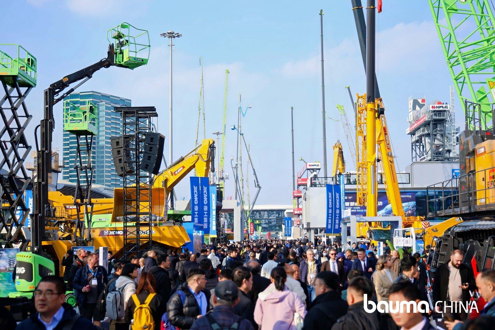 Many people walk through an outdoor exhibition area with construction machines, cranes, and information signs.